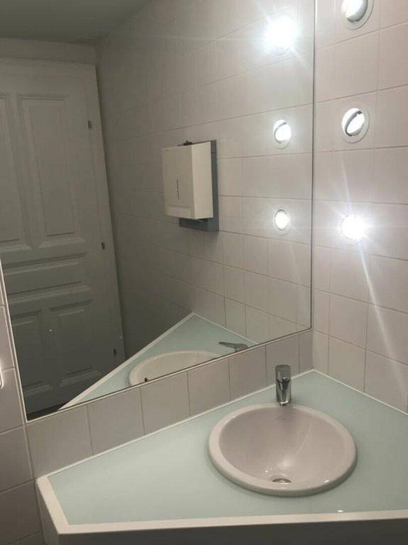 Badezimmer mit Waschbecken, großem Spiegel und hellen Fliesen an den Wänden.