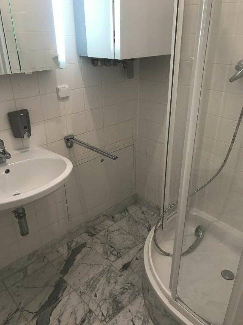 Badezimmer mit Waschbecken, Duschkabine, weißen Fliesen und Marmoroptik-Bodenfliesen.
