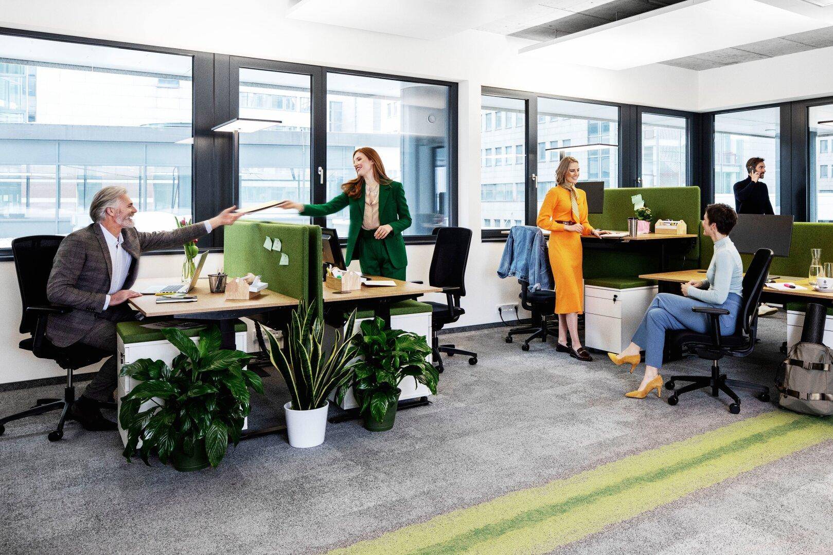Lebhaftes Büro mit grünen Akzenten, modernen Arbeitsplätzen und viel Tageslicht.