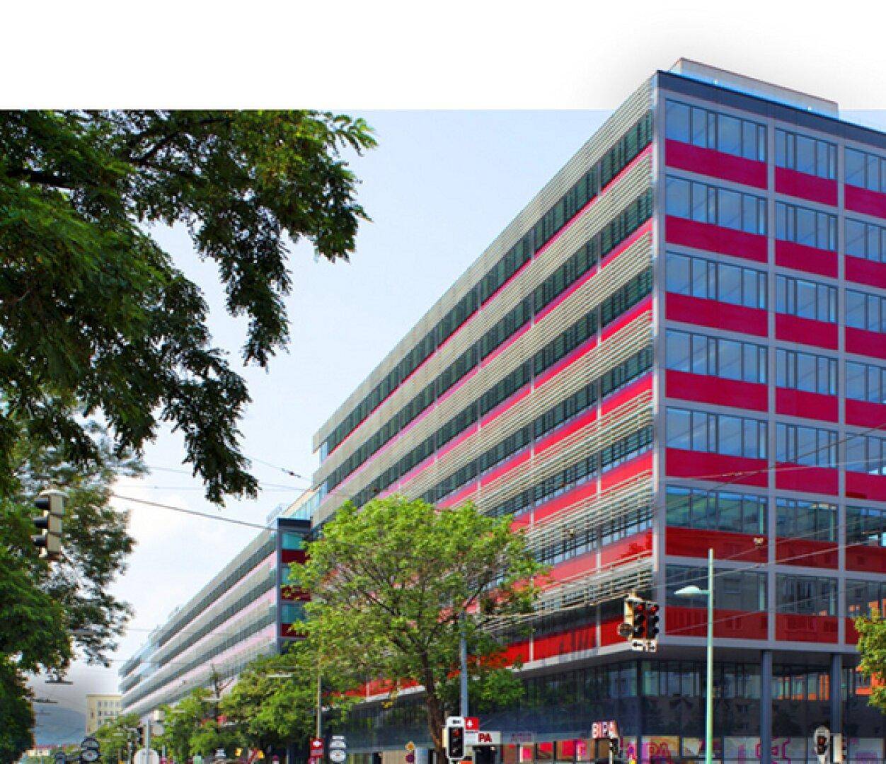 Großes, modernes Bürogebäude mit markanter roter Fassade und vielen Fenstern an einer belebten Stadtstraße.