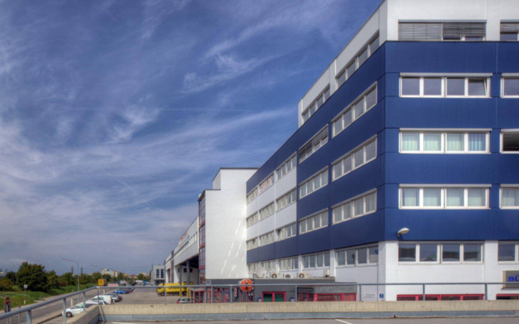 Modernes Bürogebäude mit blauer und weißer Fassade unter einem bewölkten Himmel.
