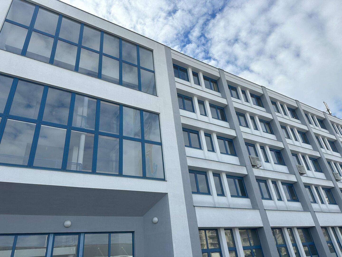 Moderne Bürogebäude-Fassade mit großen blauen Fenstern und klarem Himmel im Hintergrund.