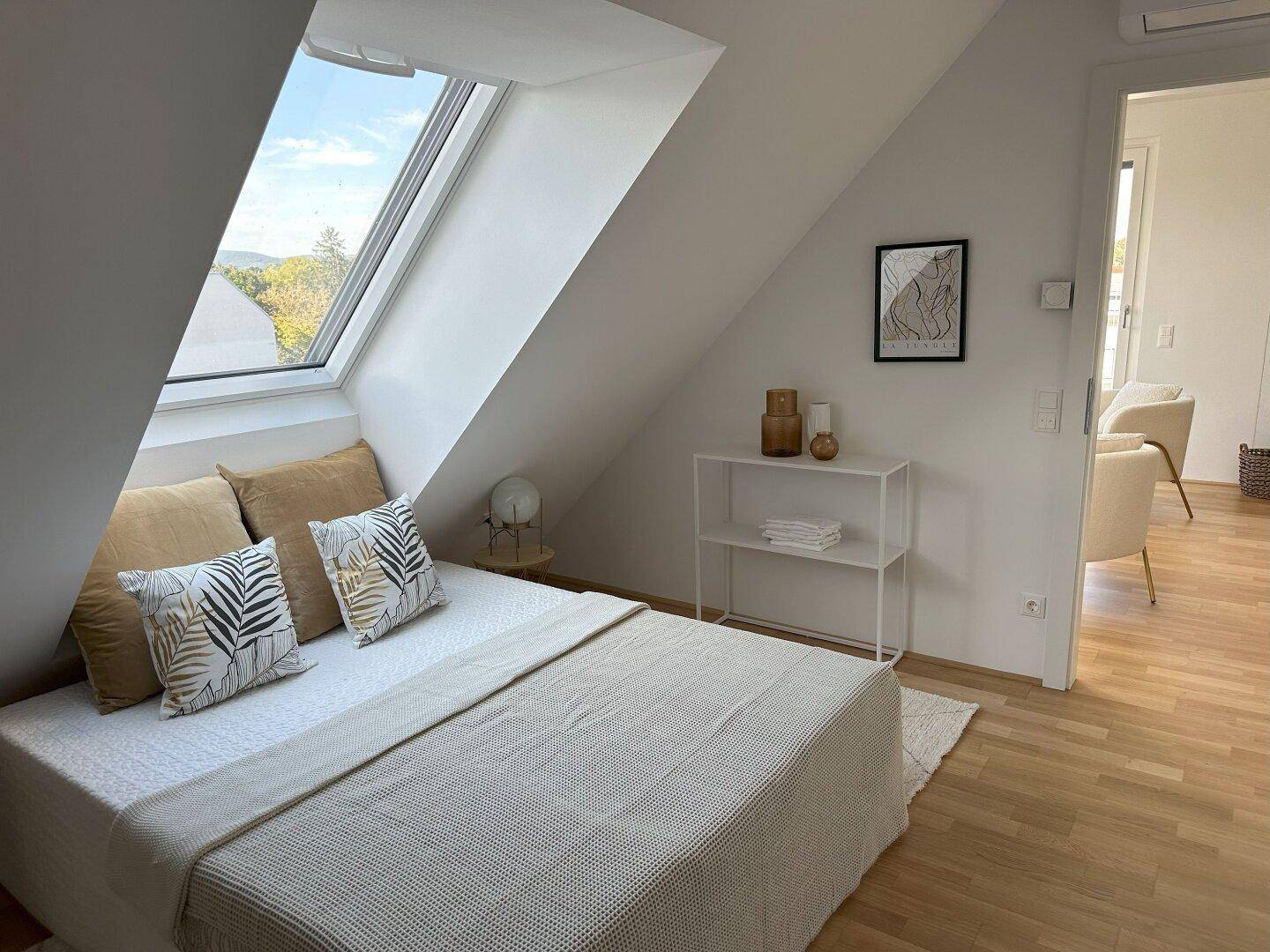 Schlafzimmer mit Dachfenster, Holzboden und Blick auf die grüne Umgebung.