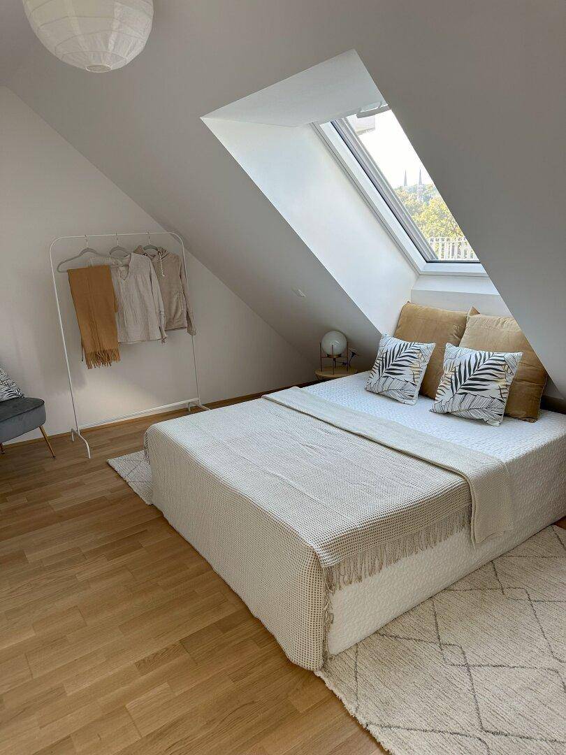 Helles Schlafzimmer mit Dachfenster, Holzboden und minimalistischer Einrichtung.
