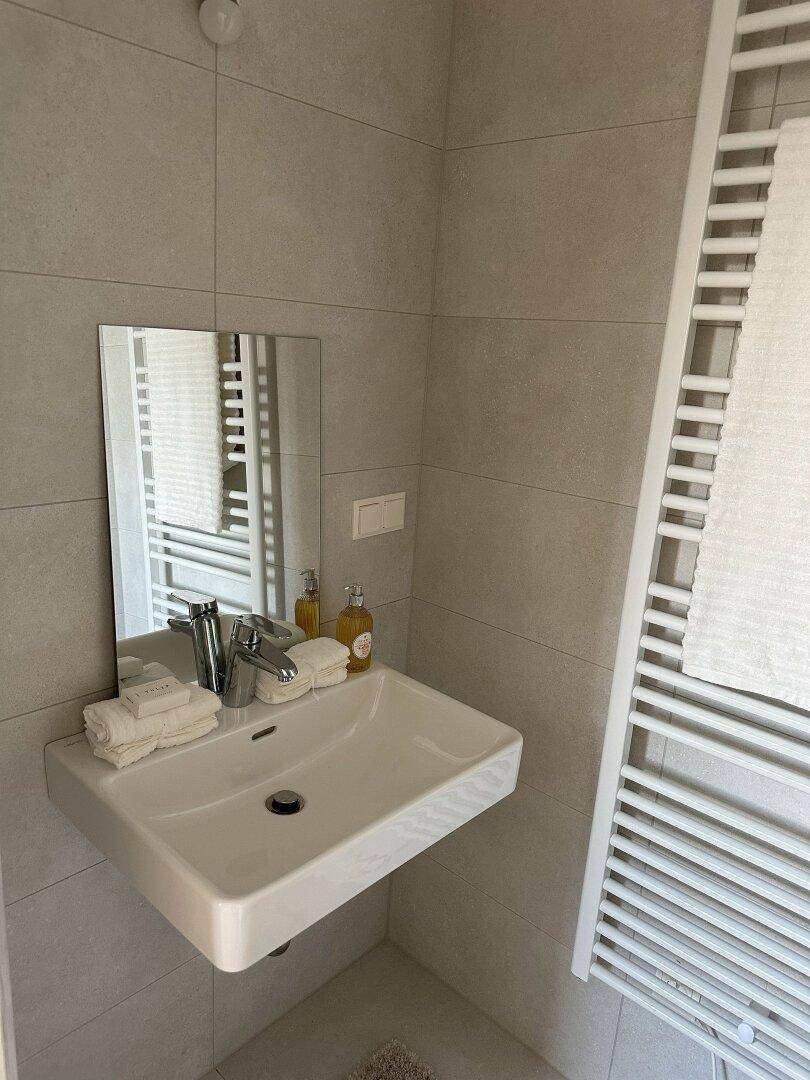 Modernes Badezimmer mit grauen Fliesen, Einzelwaschbecken und beheiztem Handtuchhalter.