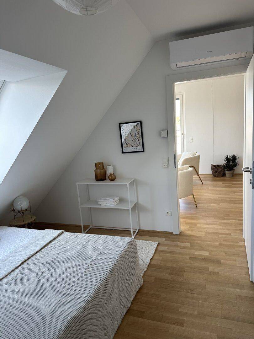 Schlafzimmer mit Holzboden, Dachschräge und Klimaanlage, verbunden mit dem Wohnbereich.