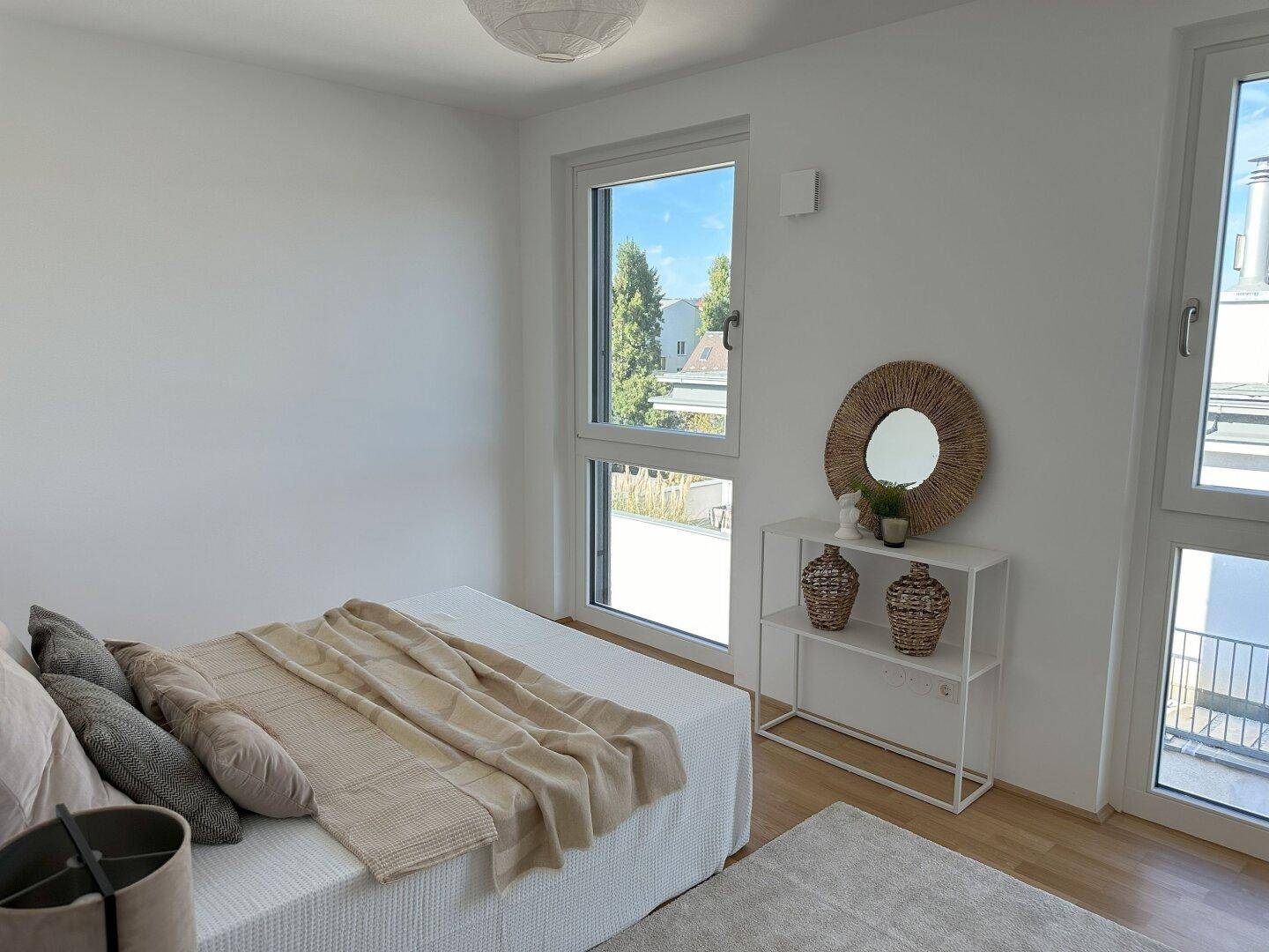 Helles Schlafzimmer mit Holzboden und großen Fenstern mit Blick ins Grüne.