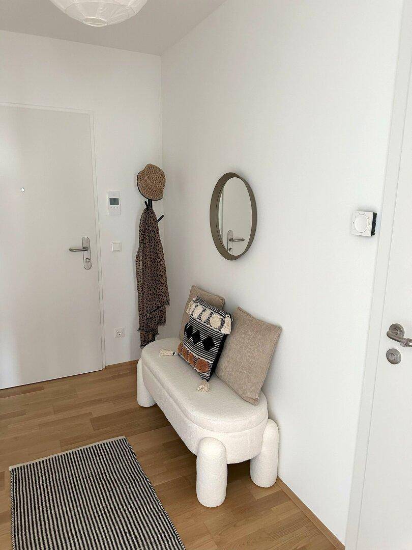 Heller Eingangsbereich mit Holzboden, Garderobe und modernem Sitzmöbel.