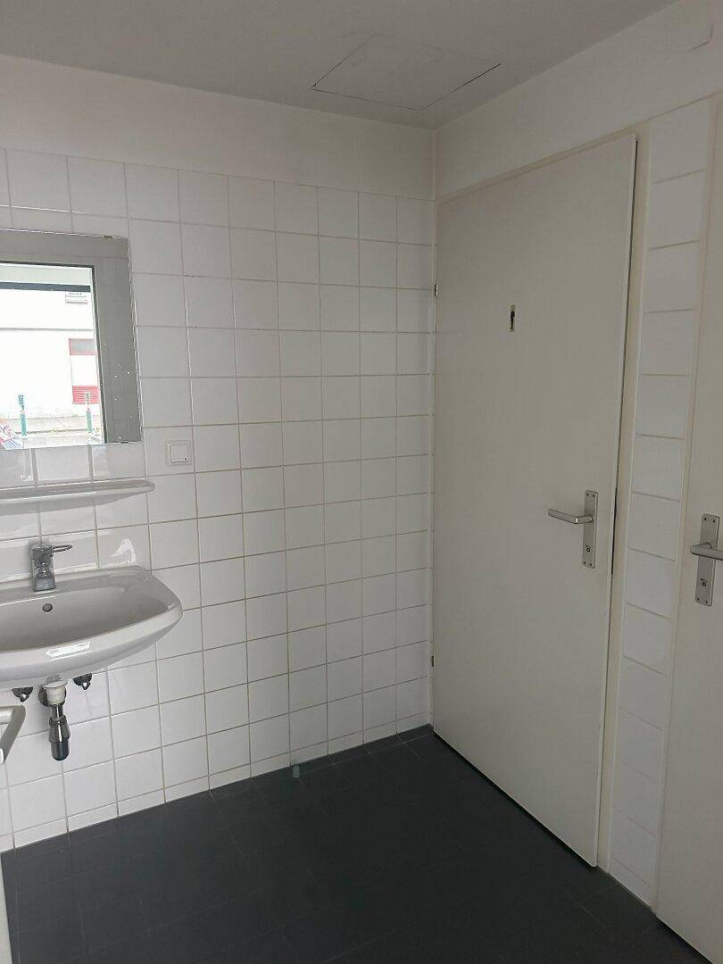 Einfacher Toilettenraum mit Waschbecken, Spiegel und weißen Wandfliesen, funktional und sauber.