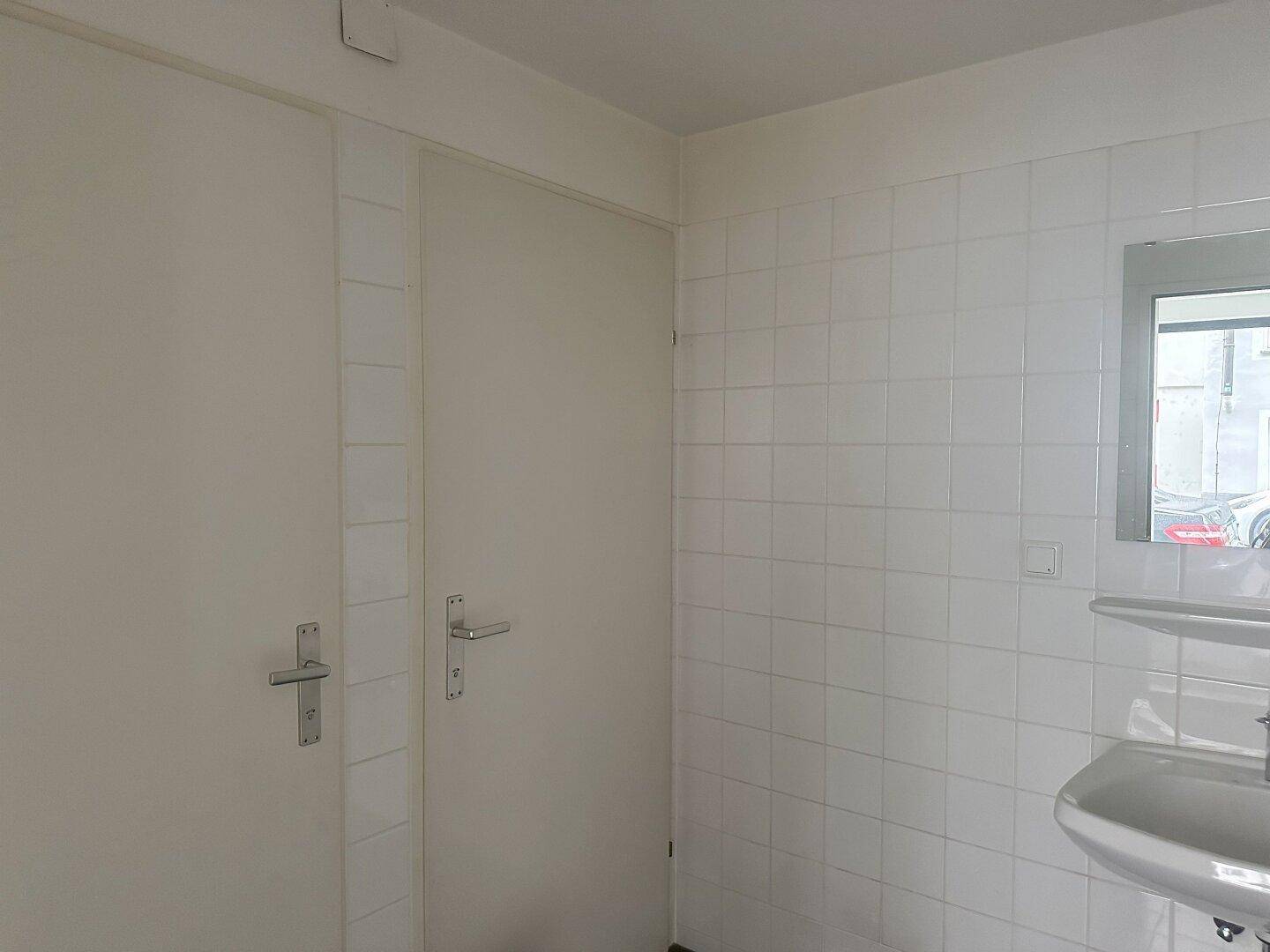 Toilettenraum mit zwei Türen, Waschbecken und weißen Fliesen, praktisch für gewerbliche Nutzung.