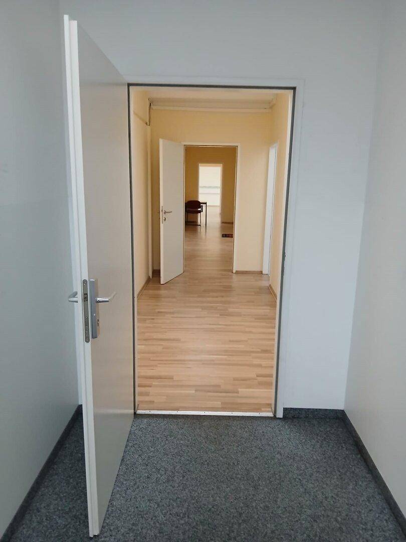 Langer Flur mit mehreren offenen Türen, der zu verschiedenen Büroräumen mit Laminatboden führt.