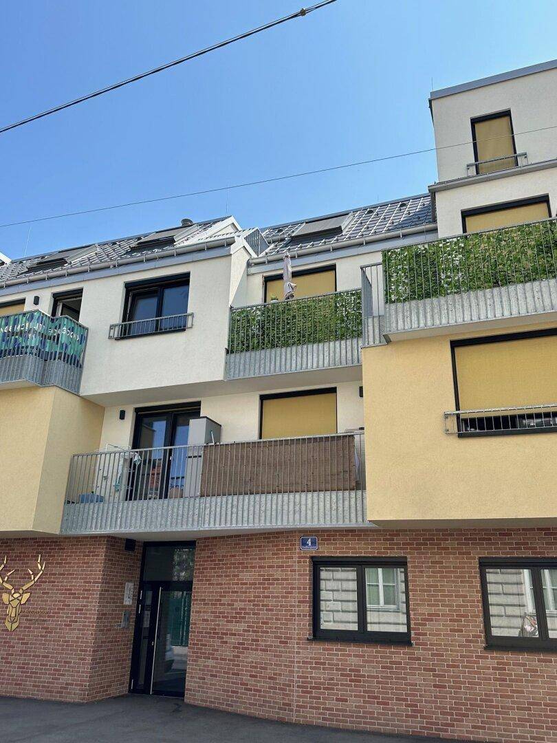 Moderne Wohnhausfassade mit Balkonen, großen Fenstern und Ziegelmauerwerk im Erdgeschoss.