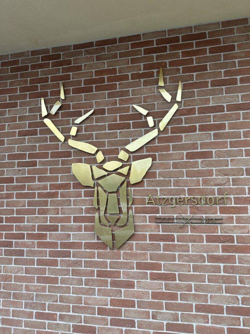Dekorative Hirschkopf-Skulptur aus Metall an einer Ziegelwand mit dem Schriftzug "Atzgersdorf".