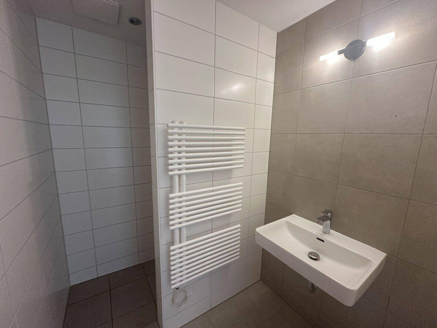 Modernes Badezimmer mit Waschbecken, beheiztem Handtuchhalter und gefliester Duschkabine in neutralen Farben.