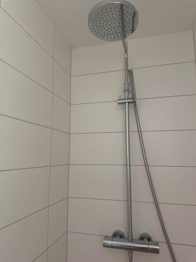 Detailaufnahme einer modernen Regendusche in einer hell gefliesten Duschkabine.