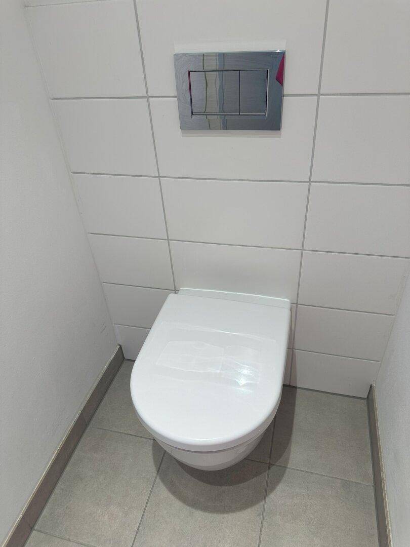 Modernes wandhängendes WC mit Spülkasten und Fliesen an den Wänden in einem Badezimmer.
