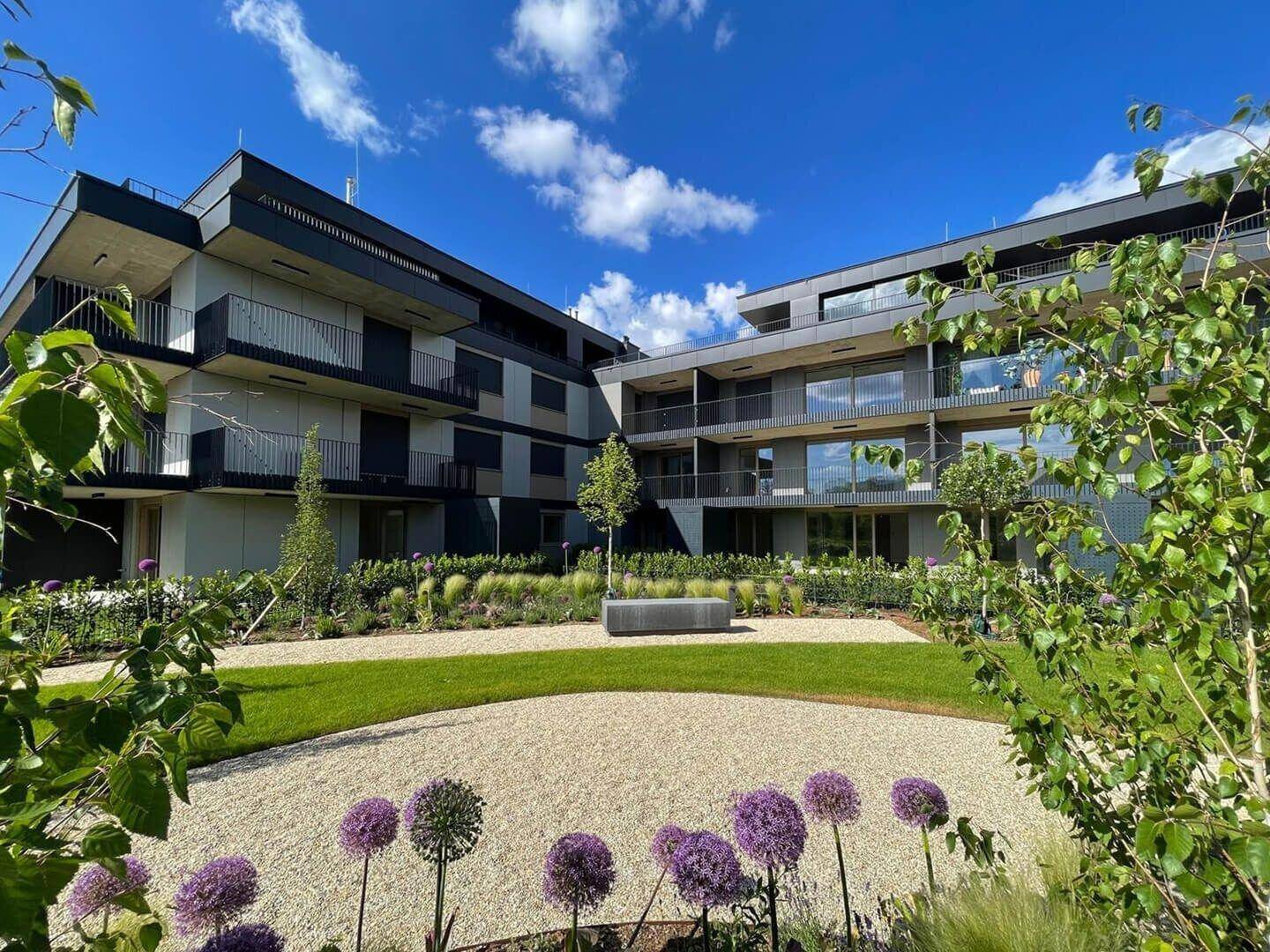 Moderne Wohnanlage mit gepflegten Grünflächen und ansprechenden Fassaden unter blauem Himmel.