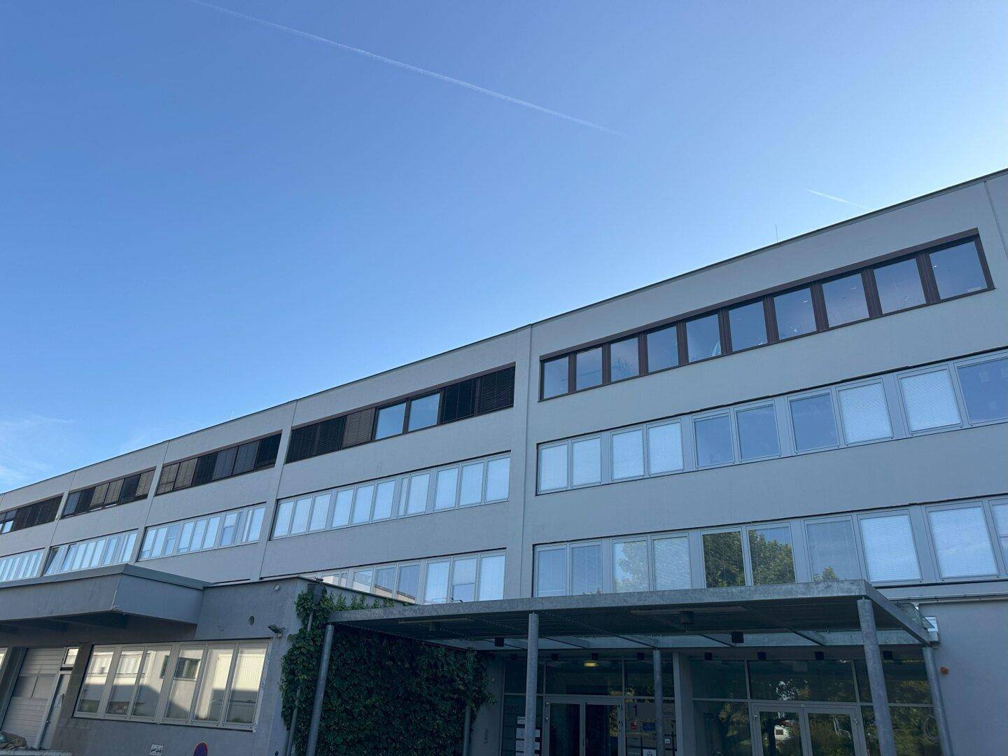 Moderne Fassade eines Bürogebäudes mit vielen Fenstern und klarem blauem Himmel.