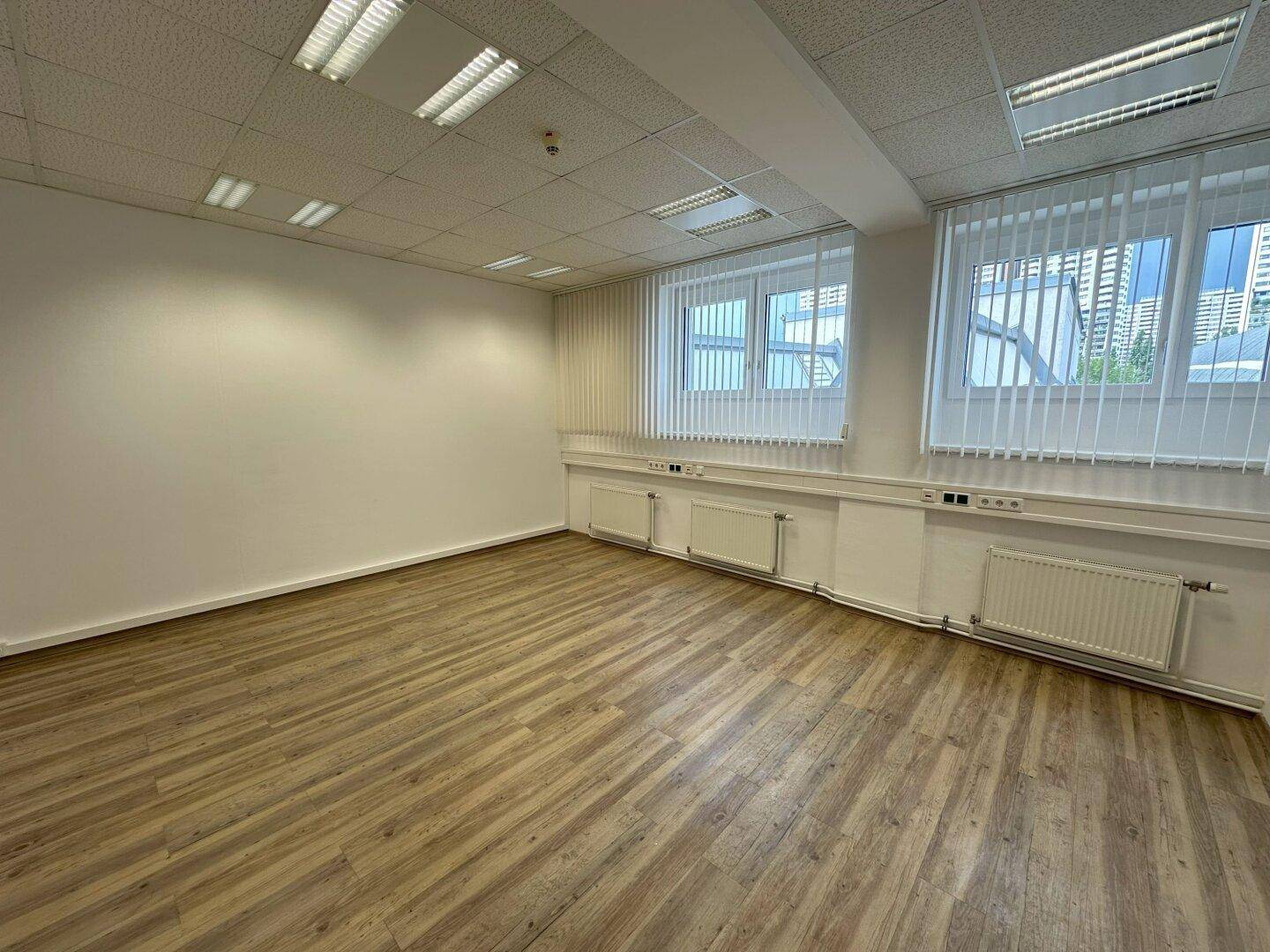 Leeres Büro mit Fenstern, die mit Jalousien ausgestattet sind, und Heizkörpern unter den Fensterbänken.