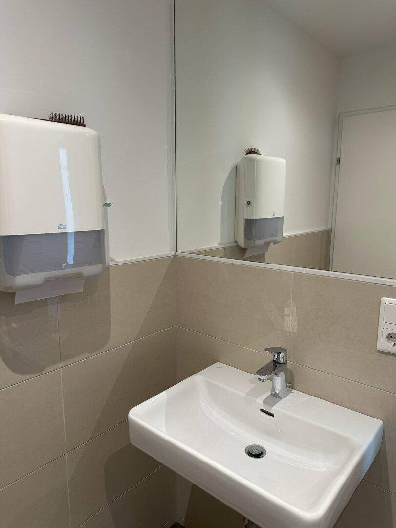 Modernes Badezimmer mit einem Waschbecken, großem Spiegel und einem Spender für Papierhandtücher.
