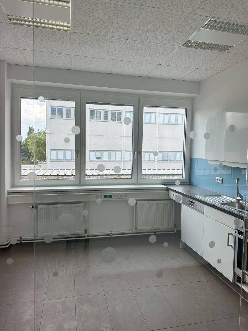 Moderne Küchenzeile hinter einer Glaswand mit weißen Schränken, blauer Rückwand und Spülmaschine.