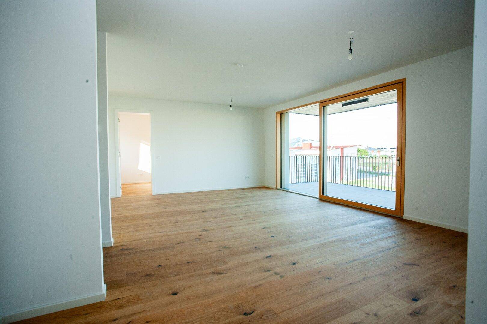 Heller, leerer Wohnraum mit Eichenparkettboden und großem Schiebefenster zum Balkon.