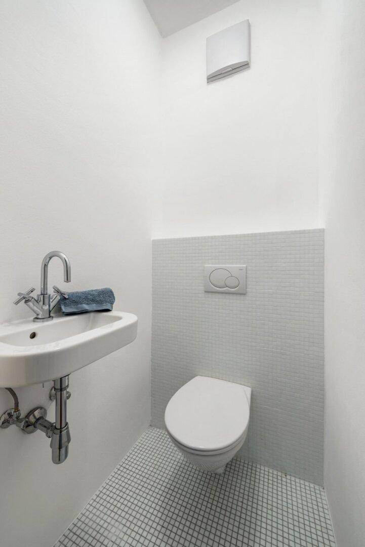 Modernes Gäste-WC mit weißen Mosaikfliesen, wandhängendem WC und kleinem Waschbecken.