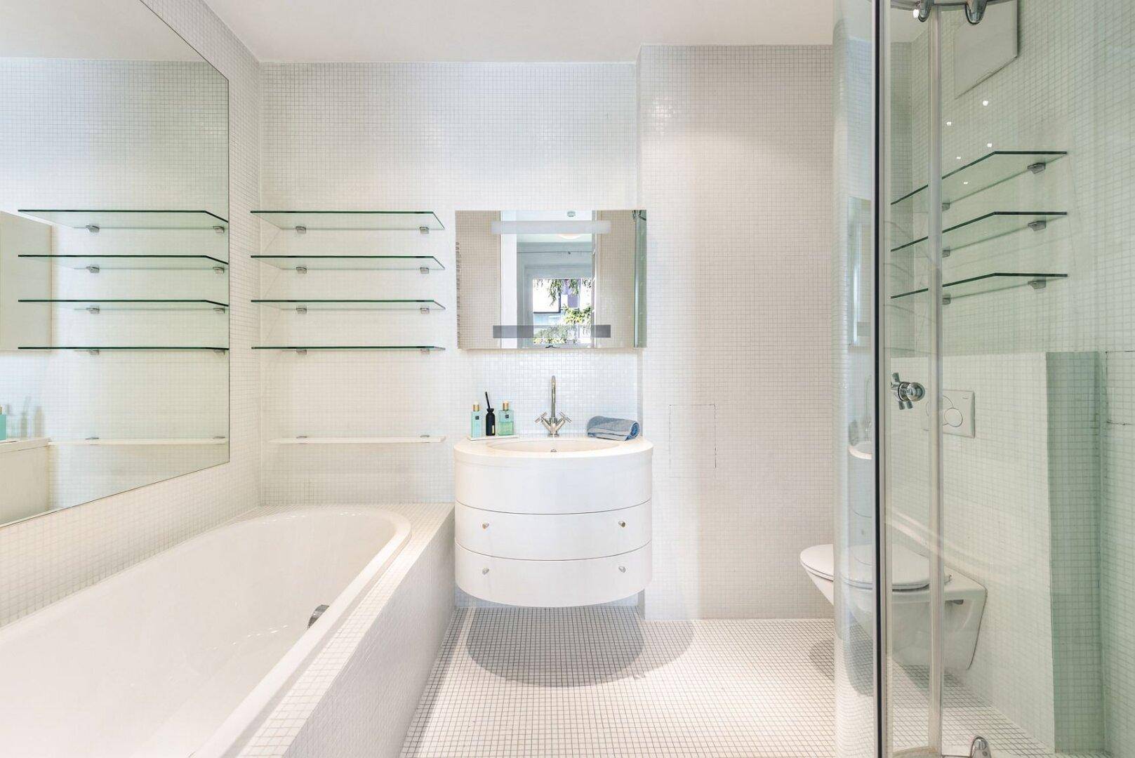 Modernes Badezimmer mit weißen Mosaikfliesen, Badewanne, Waschtisch und separater Duschkabine.