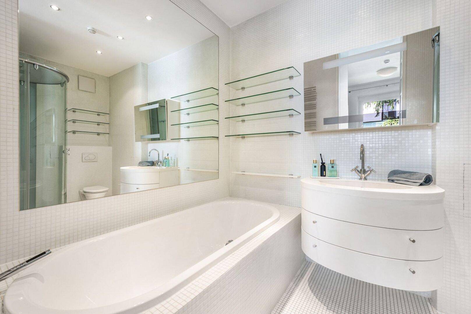 Helles Badezimmer mit großer Spiegelfläche, Badewanne, Waschtisch und Duschkabine in modernem Design.