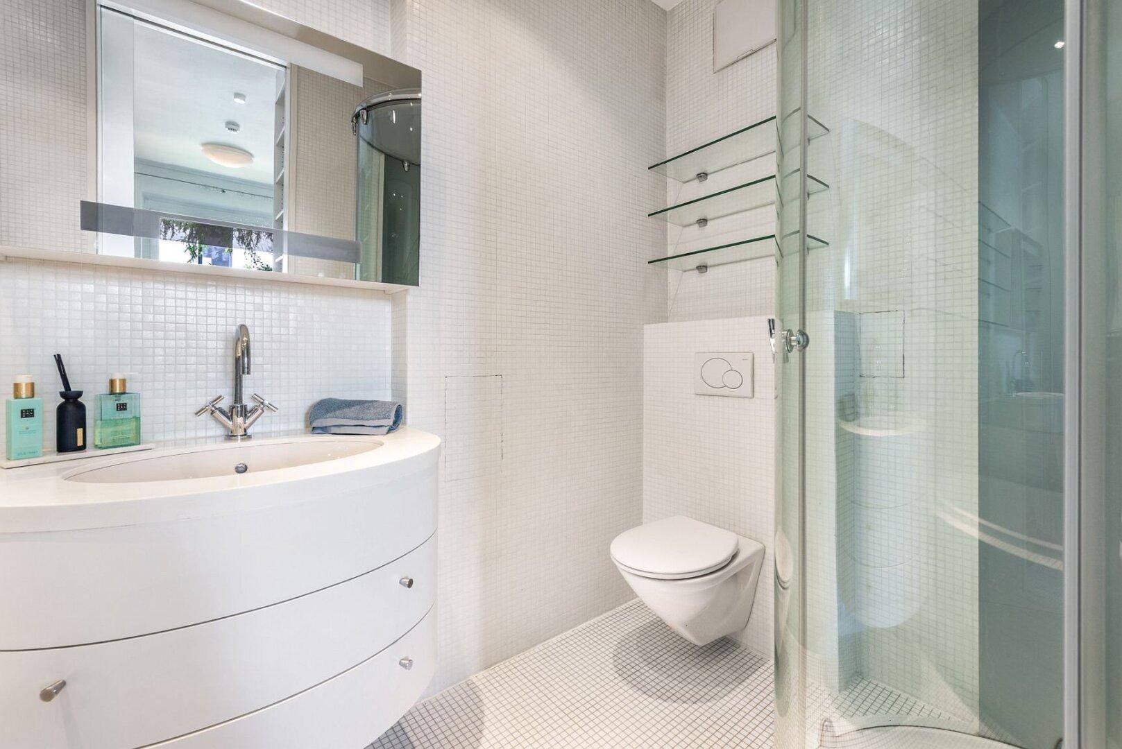 Modernes Badezimmer mit Duschkabine, wandhängendem WC und elegantem Waschtisch mit Mosaikfliesen.