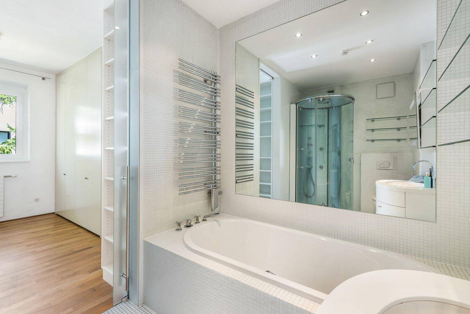 Geräumiges Badezimmer mit Badewanne, beheiztem Handtuchhalter und großem Spiegel, der den Raum erweitert.