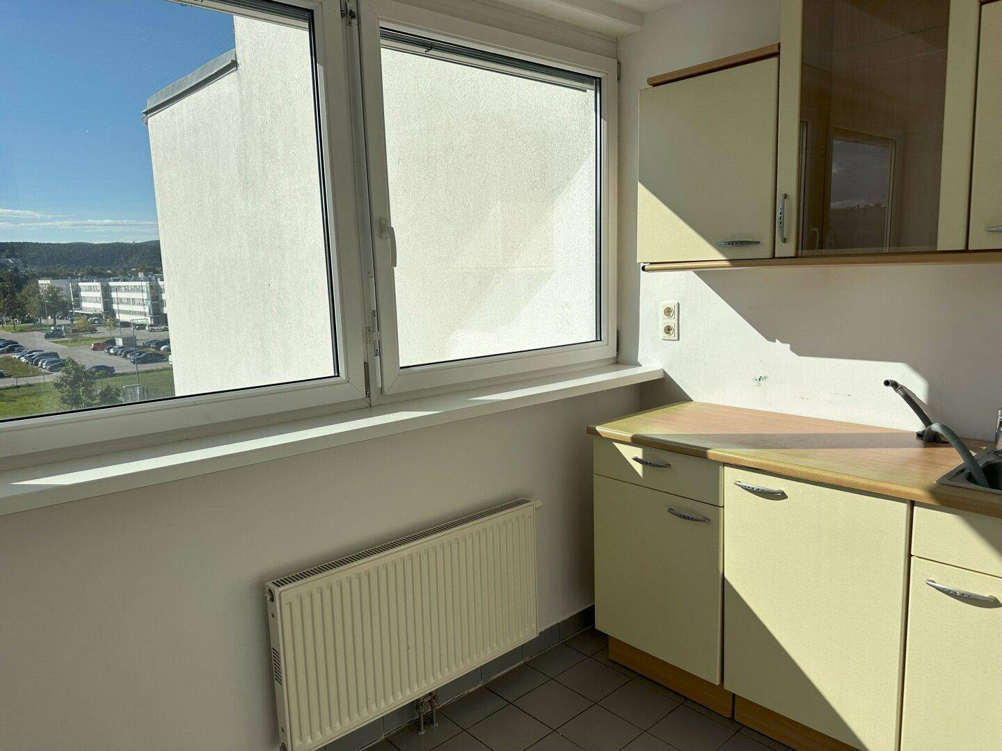 Kleine Teeküche mit Einbauschränken, Spüle und Fensterblick auf die Umgebung.
