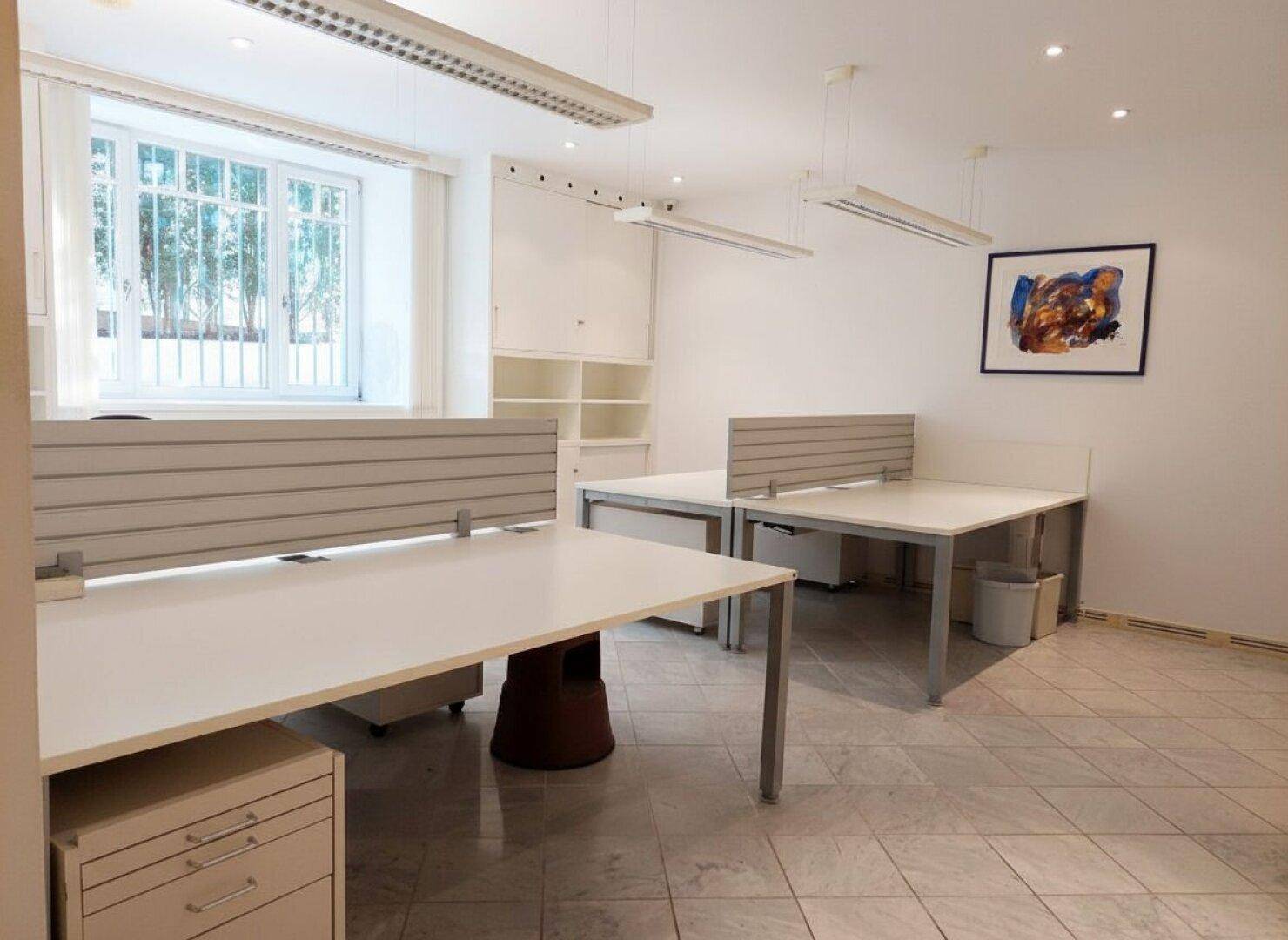 Geräumiges Büro mit mehreren Arbeitsplätzen, großen Fenstern und heller Fliesenboden.