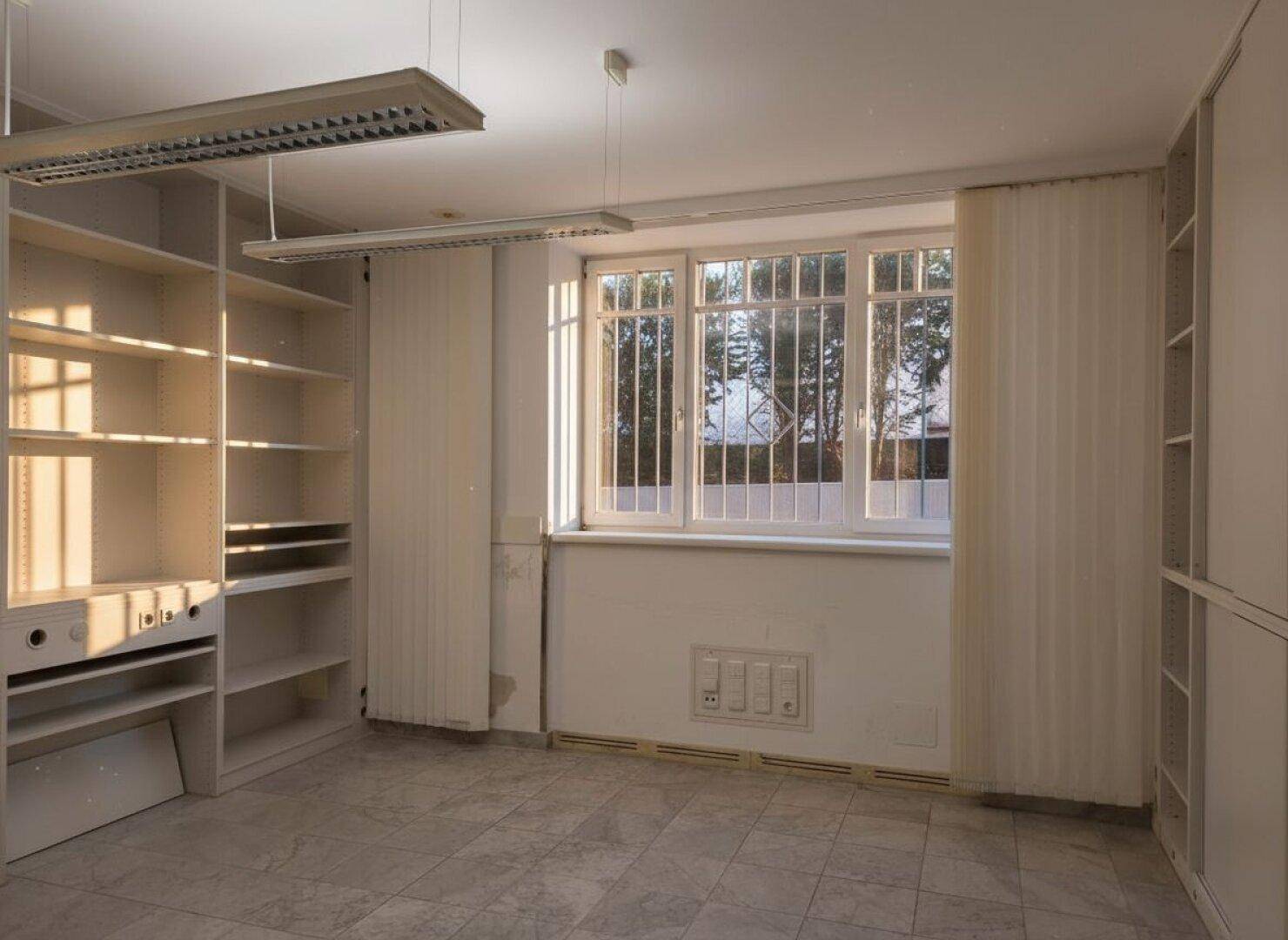 Leeres Büro mit Einbauregalen, großem Fenster und hellem Fliesenboden.