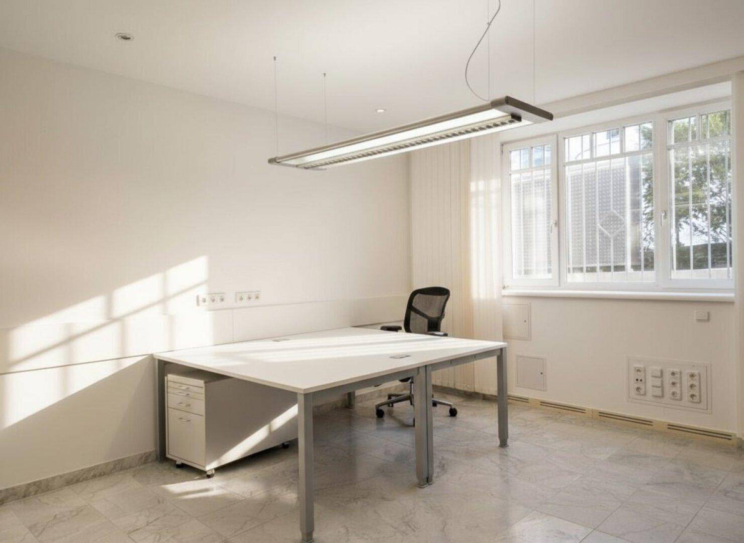 Einzelbüro mit großem Fenster, viel Tageslicht und einem modernen Schreibtisch.