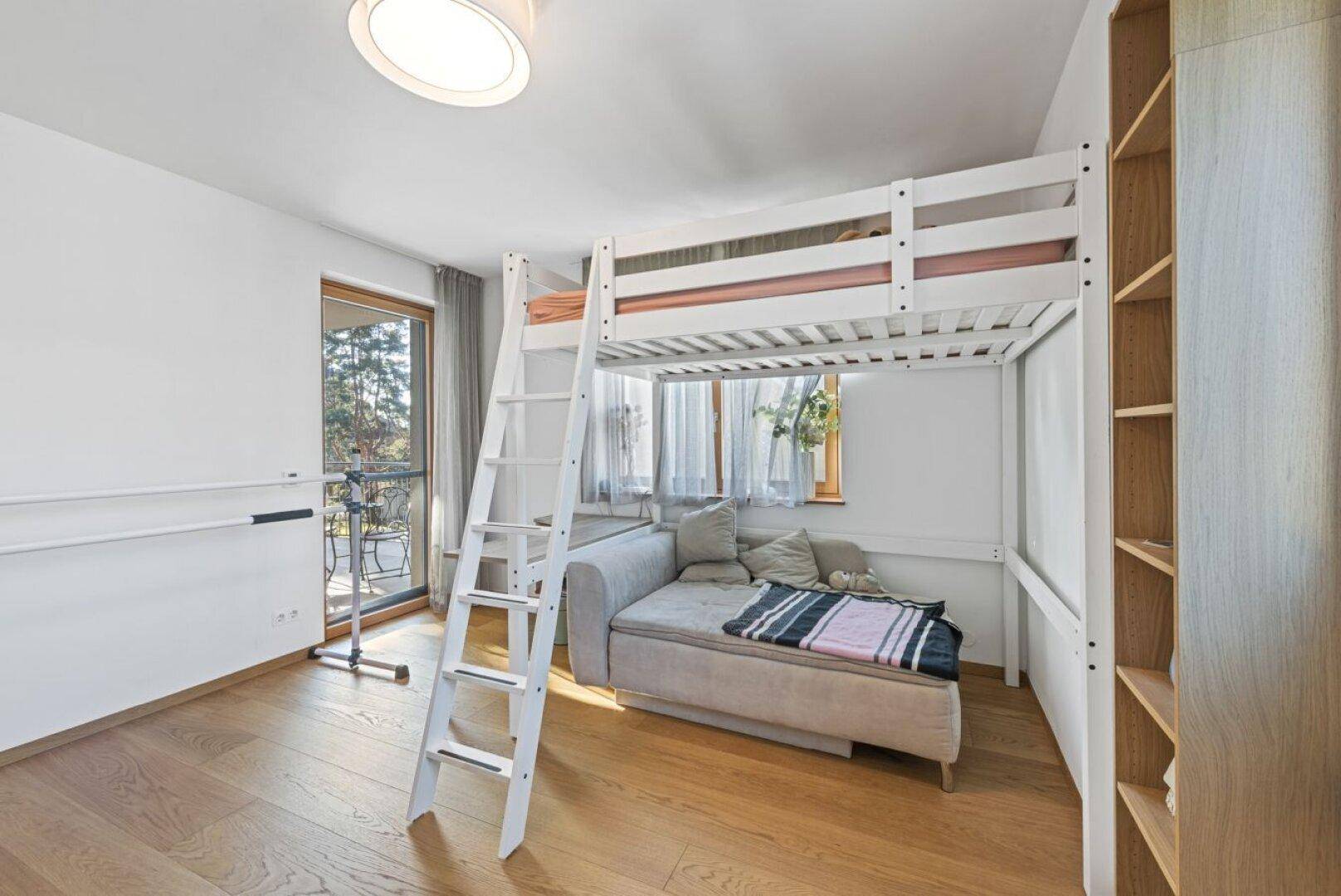 Kinderzimmer mit Hochbett, Sofa und direktem Zugang zu einem kleinen Balkon, hell und funktional eingerichtet.