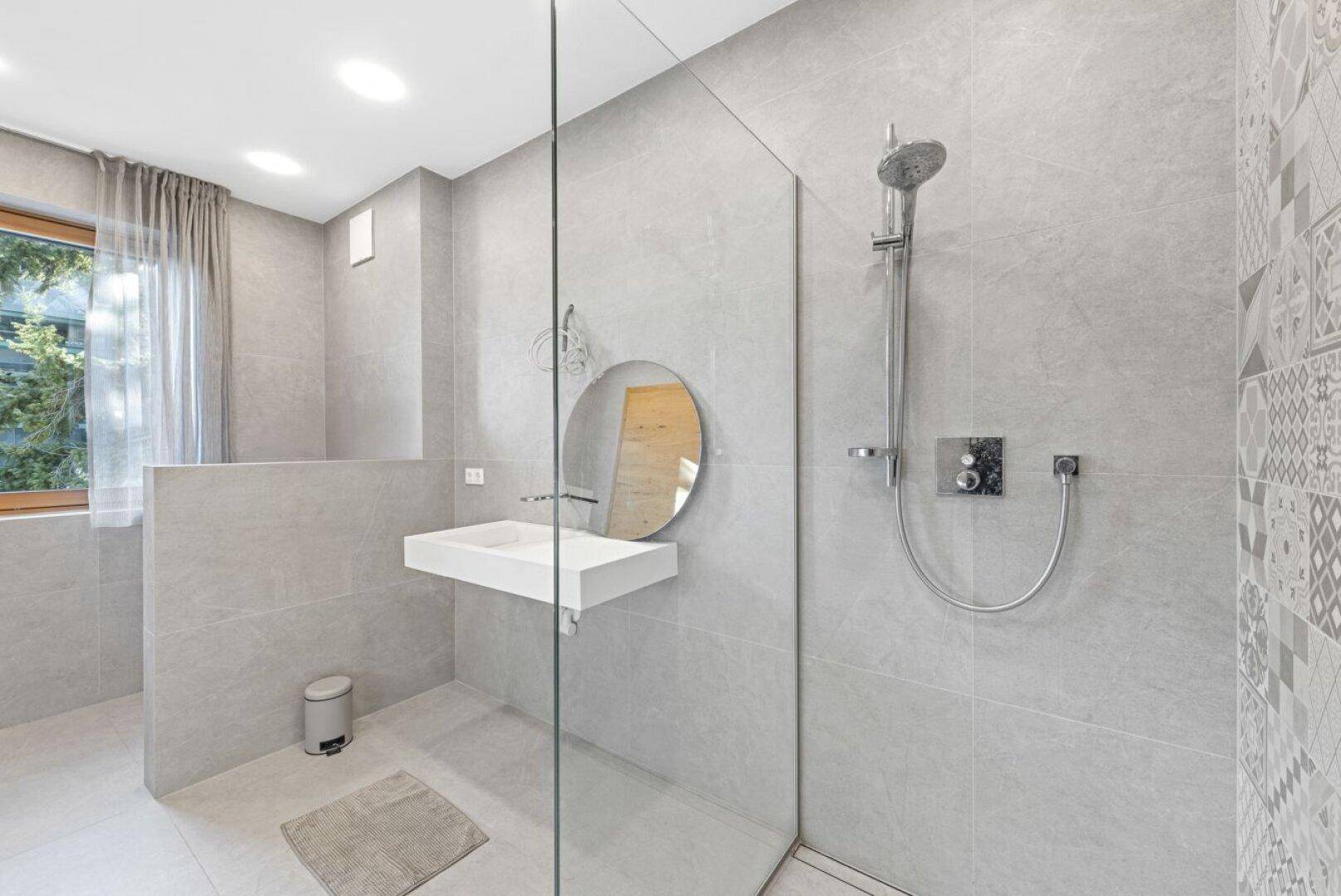 Helles Badezimmer mit begehbarer Dusche, modernem Waschbecken und Fenster, ausgestattet mit grauen Fliesen.