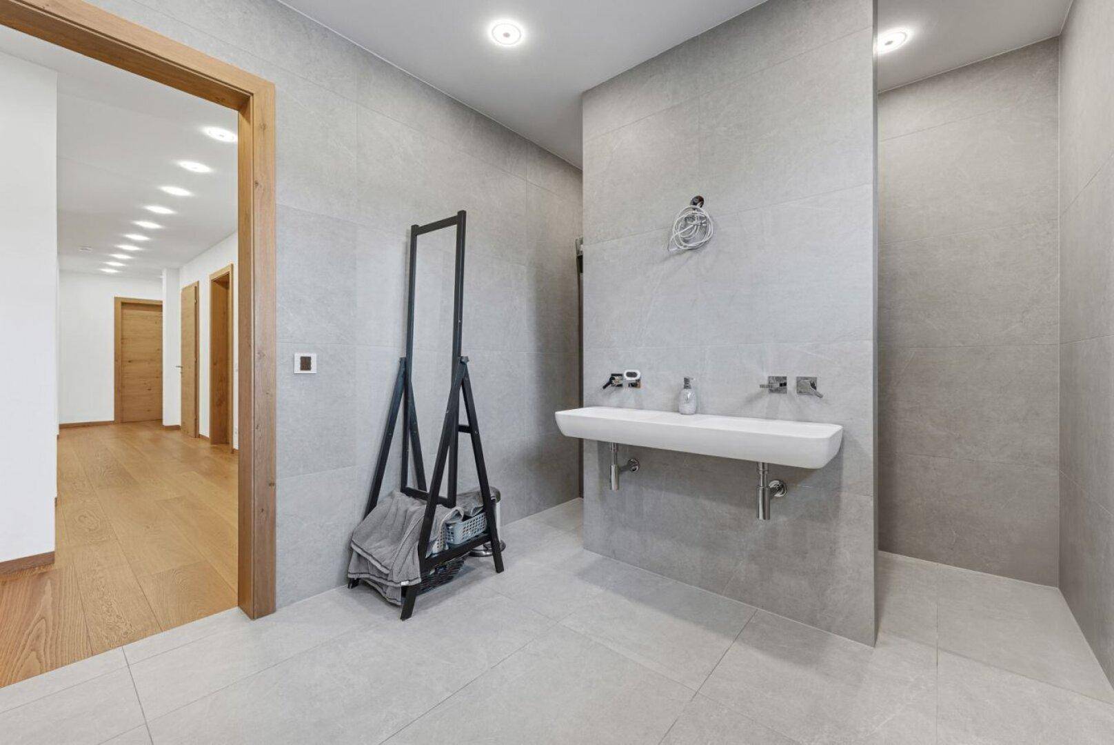 Modernes Badezimmer mit grau gefliesten Wänden, Einzelwaschbecken und Zugang zum Flur.