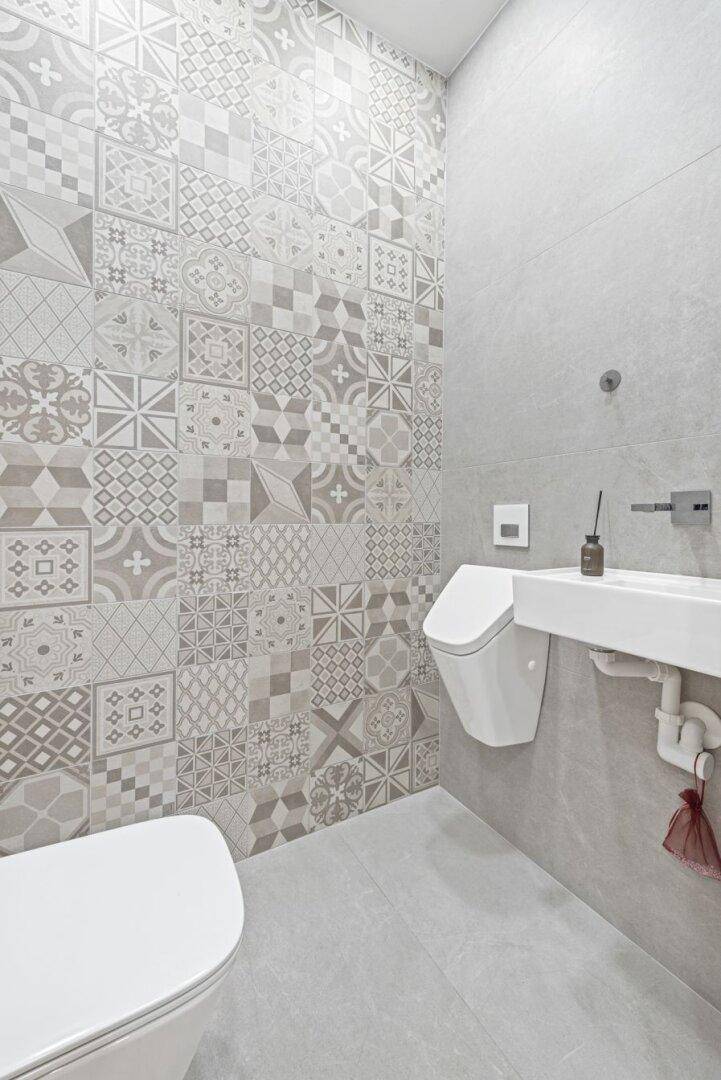 Modernes Gäste-WC mit gemusterten Fliesen, wandhängendem WC und Urinal in Grau-Tönen.