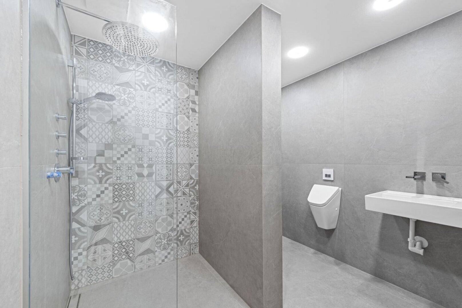 Moderne Dusche mit Regenduschkopf und gemusterten Fliesen in einem grauen Badezimmer.
