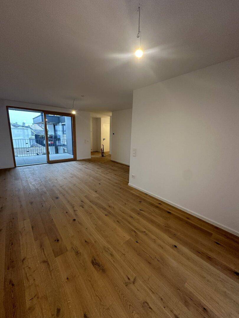 Geräumiger, heller Wohnbereich mit Holzboden und großem Fenster, das viel Tageslicht hereinlässt.