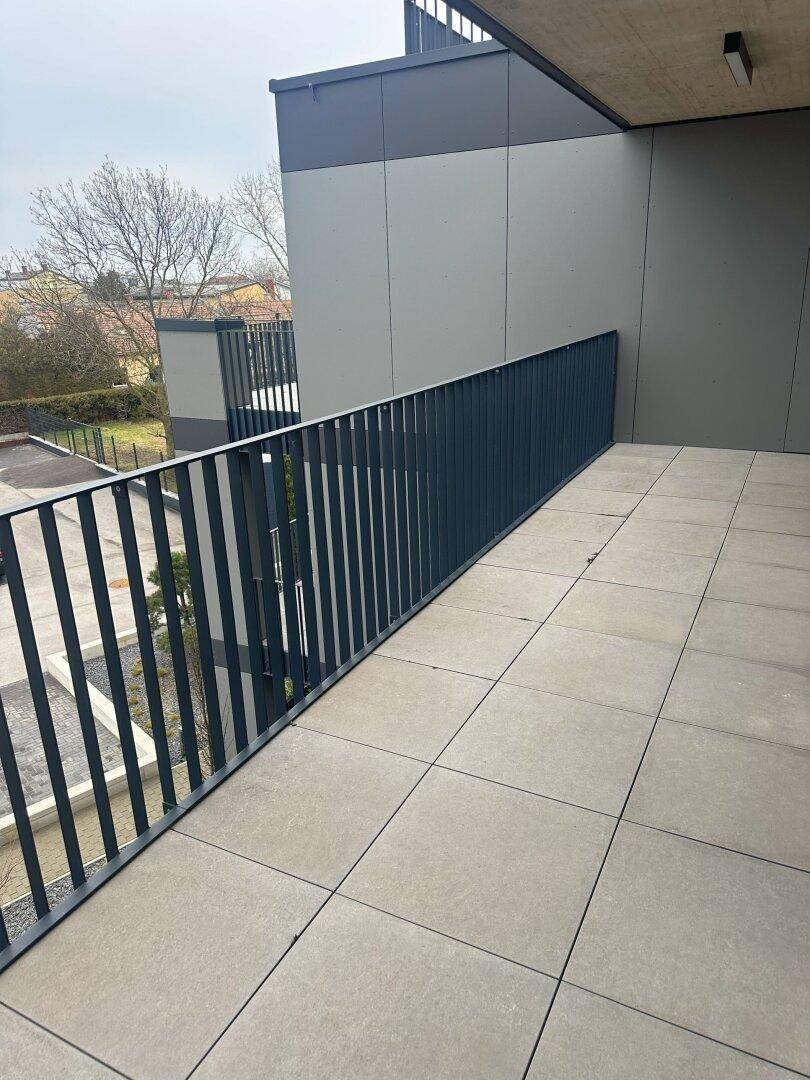 Langer, gefliester Balkon mit modernem Geländer und Blick auf die Umgebung.