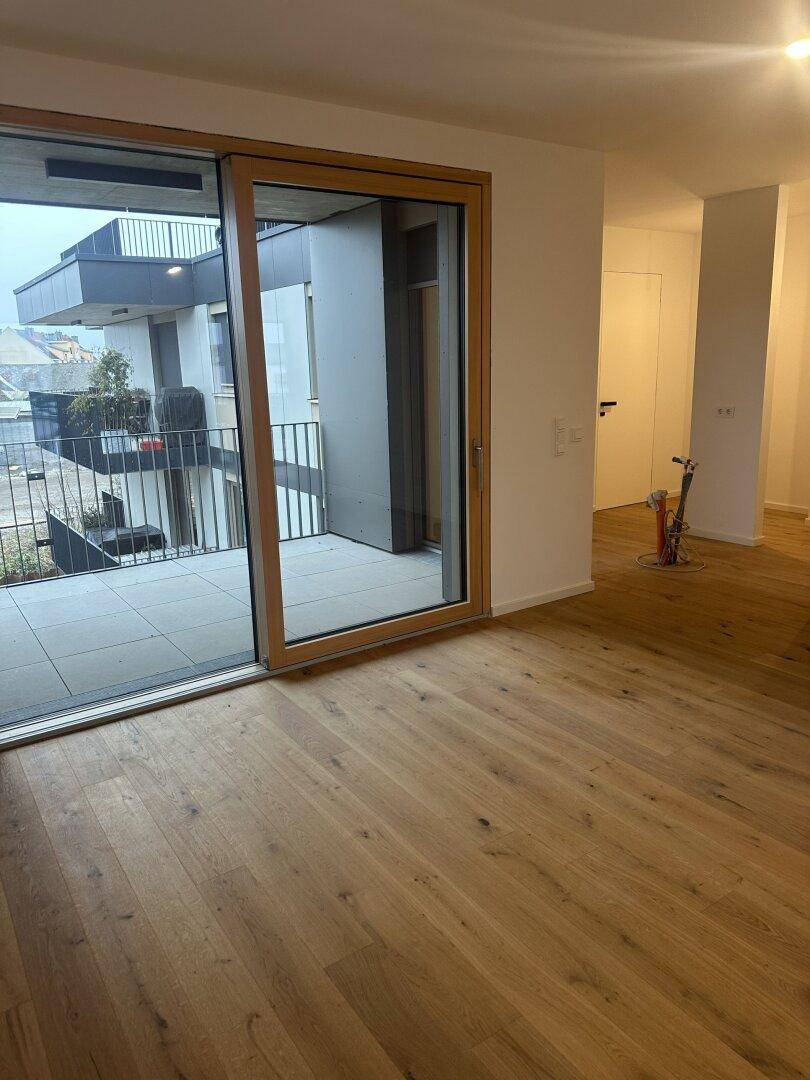 Heller Wohnbereich mit Holzboden und Zugang zu einem großzügigen Balkon.