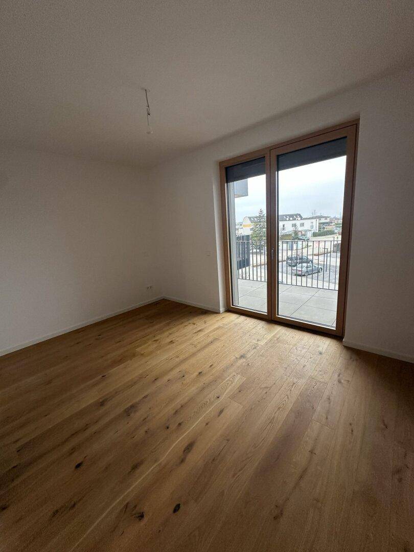 Helles Zimmer mit Holzboden und Zugang zu einem Balkon, ideal als Schlaf- oder Arbeitszimmer.