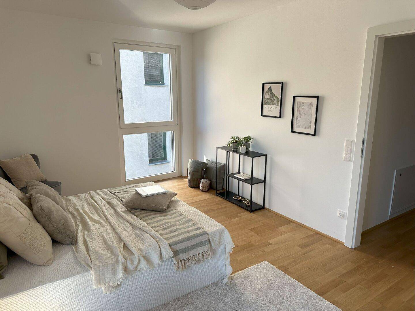 Helles Schlafzimmer mit Holzboden, großem Fenster und minimalistischer Einrichtung.