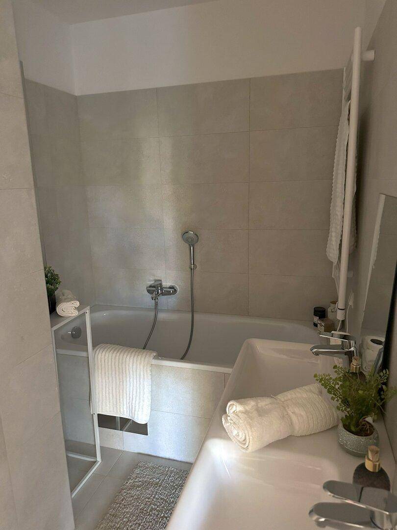Modernes Badezimmer mit Badewanne, hellen Fliesen und beheiztem Handtuchhalter.