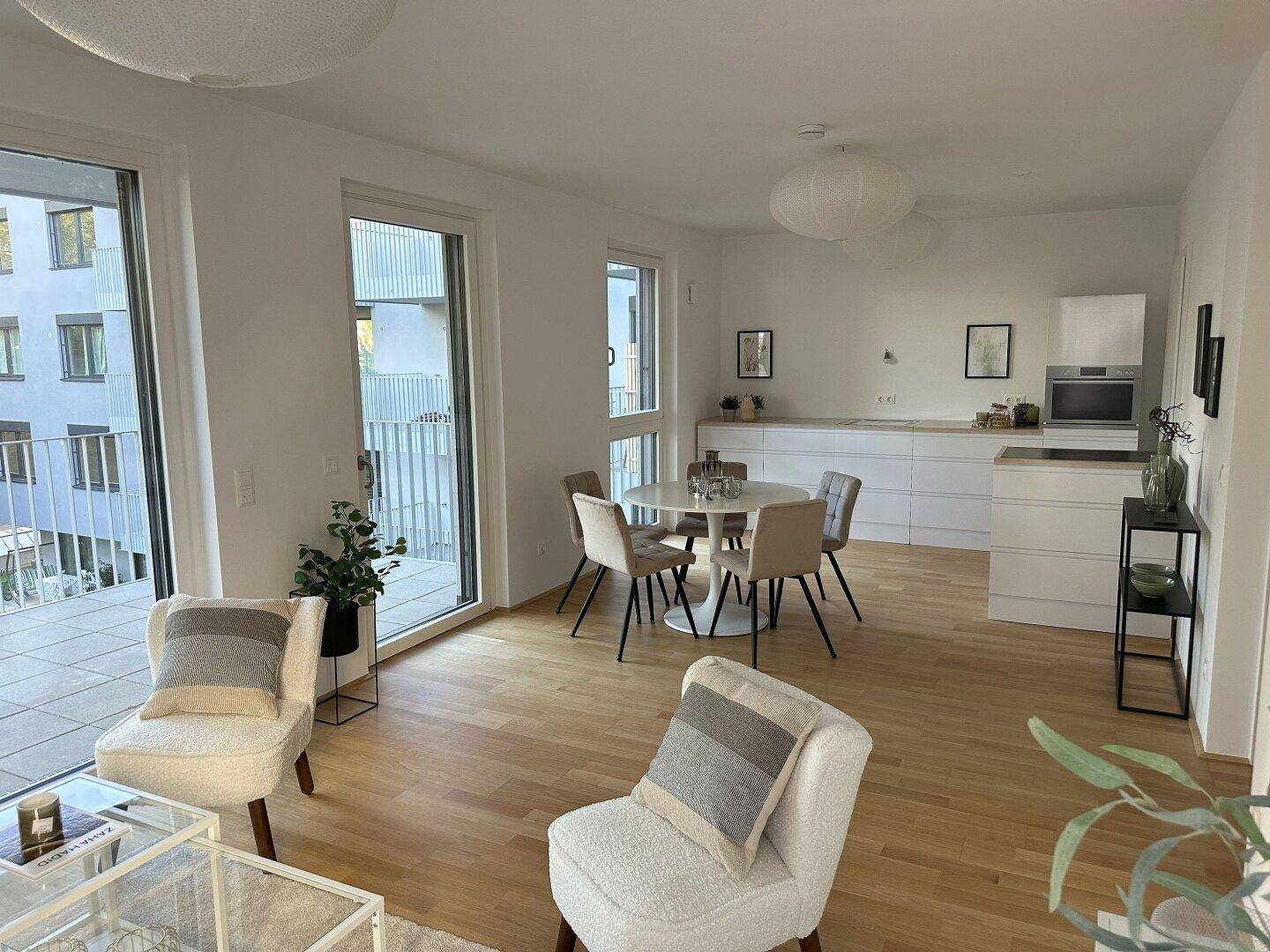 Offener Wohn-Essbereich mit Küche, Holzboden und Zugang zu einem Balkon.