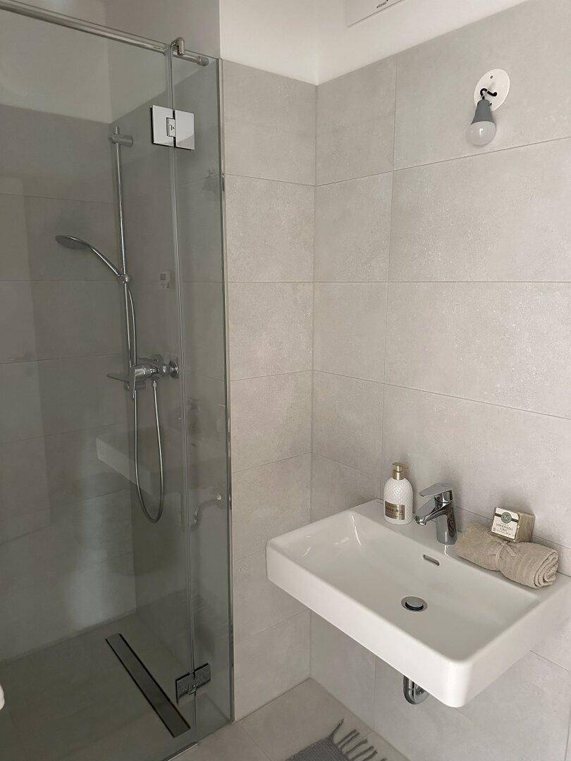 Modernes Badezimmer mit ebenerdiger Dusche, Waschbecken und hellen Fliesen.
