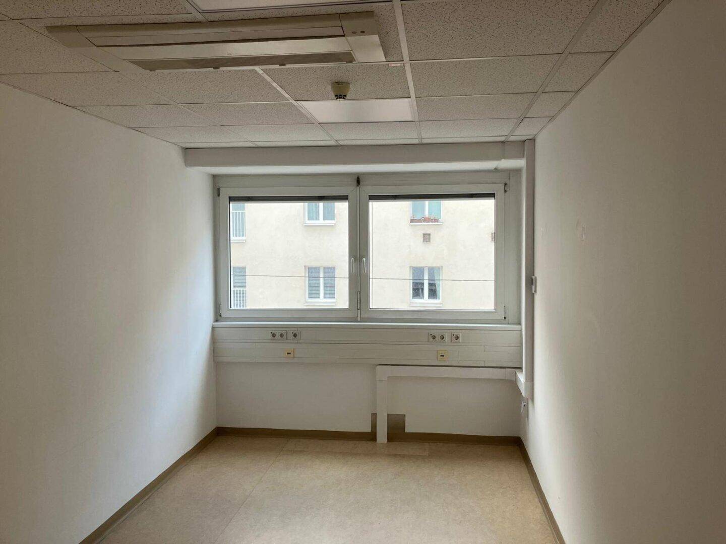 Leerer Büroraum mit einem großen Fenster, das viel Tageslicht spendet und einen Blick auf die Umgebung ermöglicht.