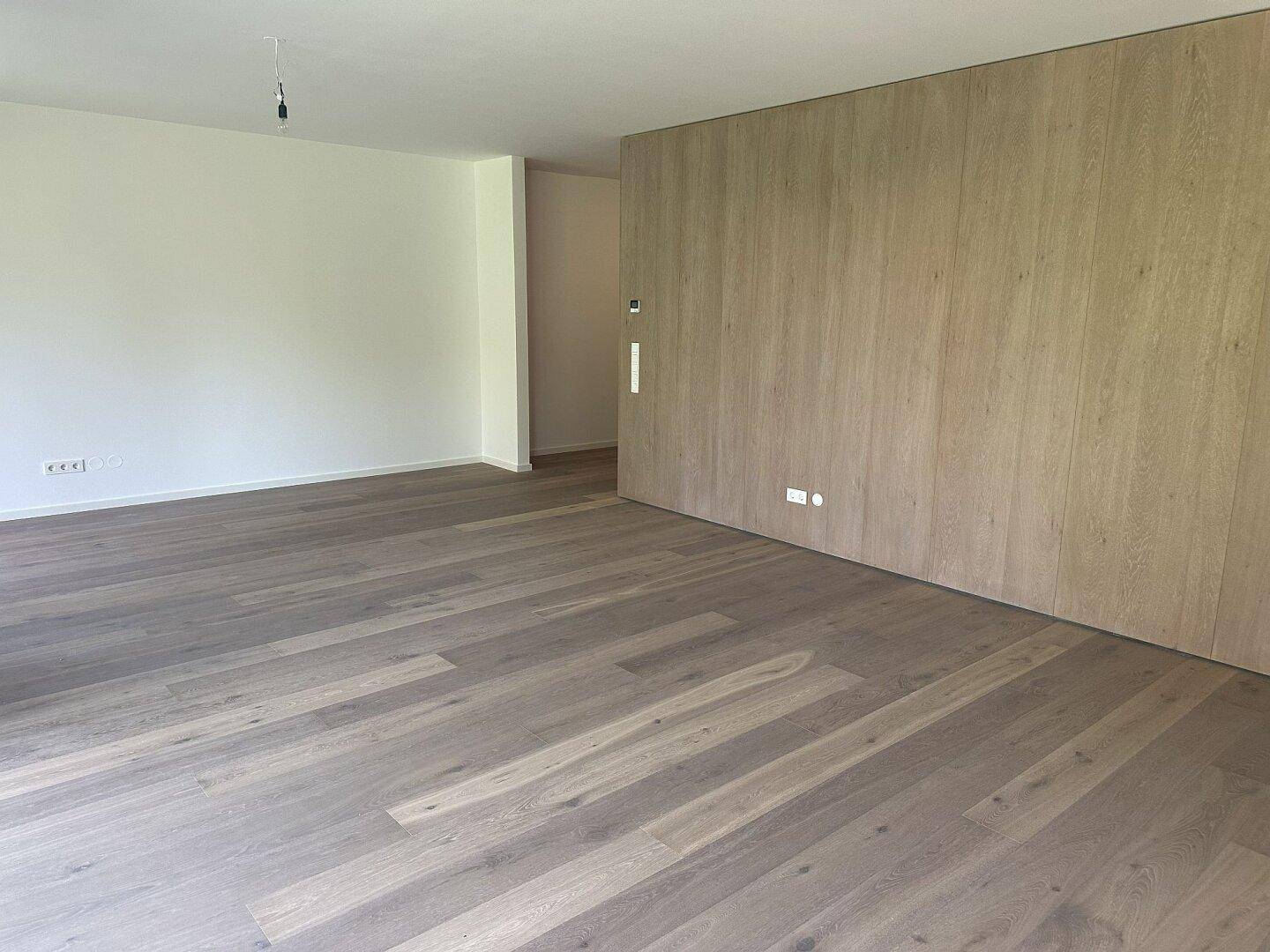Geräumiger, heller Wohnbereich mit Holzparkett und einer modernen Holzwand.